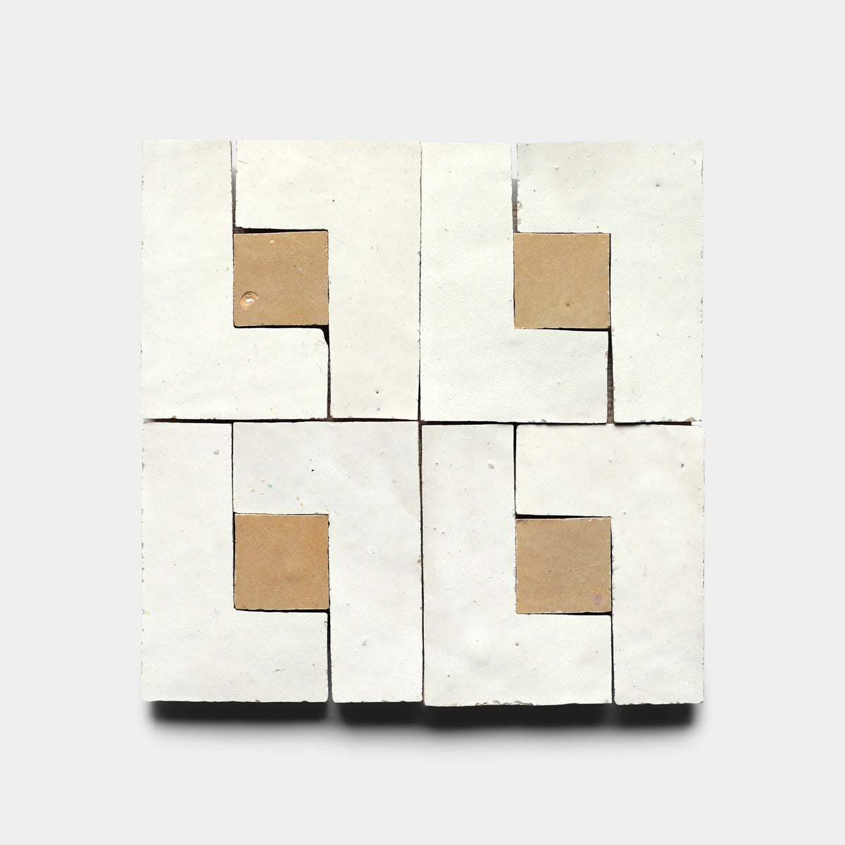Four Rubric 6, Sample tiles by Zia Tile—matte white squares with tan L-shaped sections—are arranged in a pinwheel pattern, creating a striking geometric design ideal for modern settings.