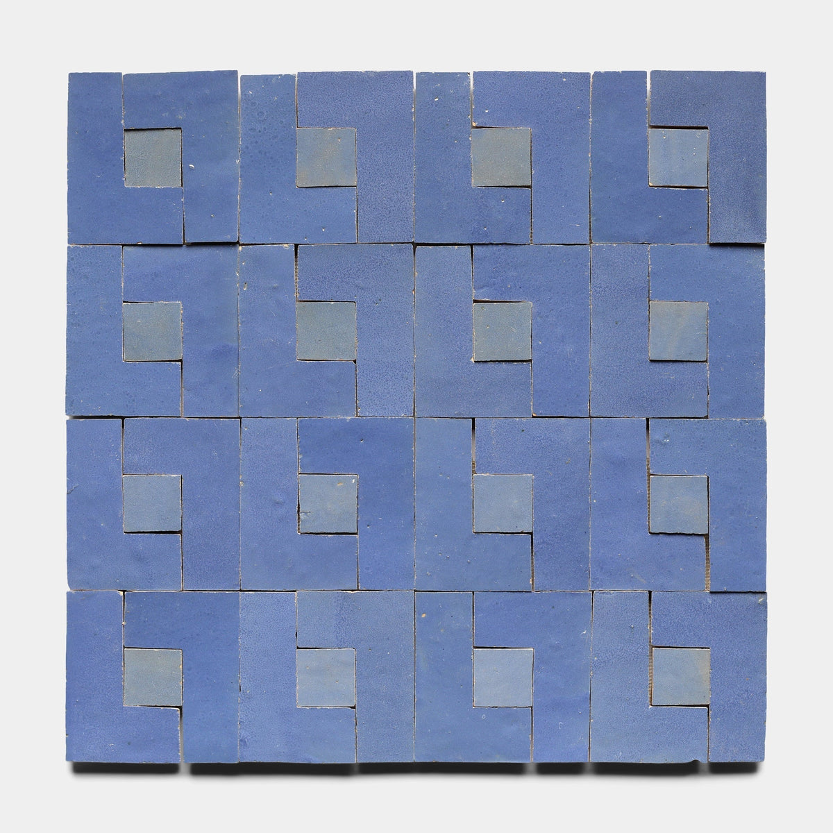 Rubric 7, Sample by Zia Tile features blue handcrafted tiles in a geometric grid, each with an L-shaped motif and square inset, forming a repeating, maze-like design inspired by classic Zia Tile cement styles.