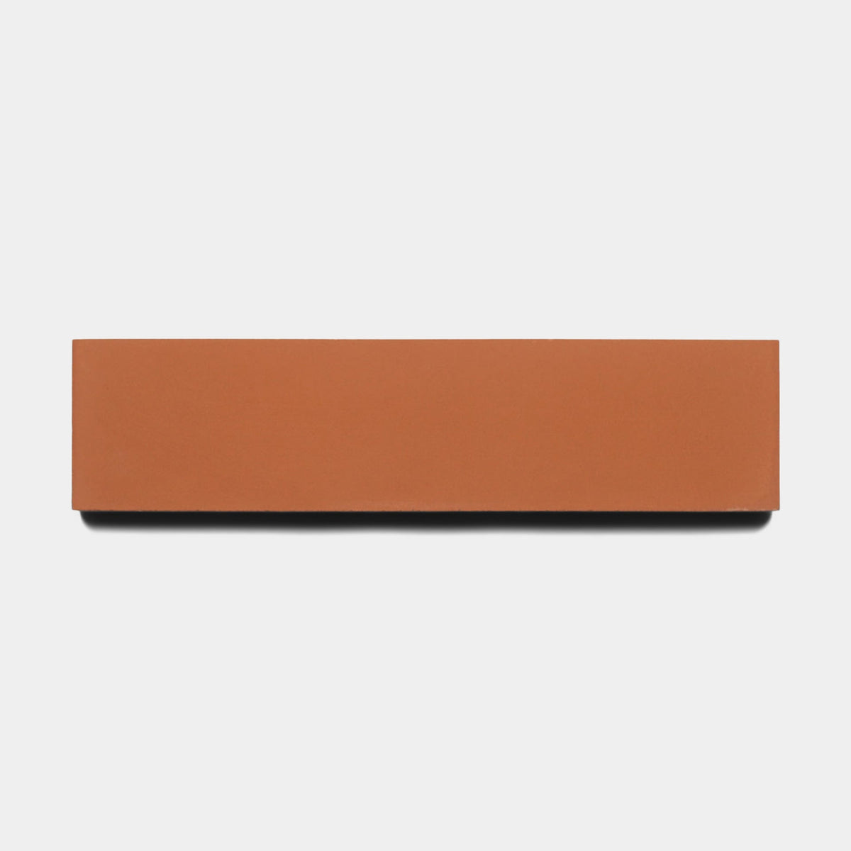 A sample of Zia Tile's Rust 2x8 brick, rectangular and reddish-brown, is displayed against a plain white background with a subtle shadow beneath it.