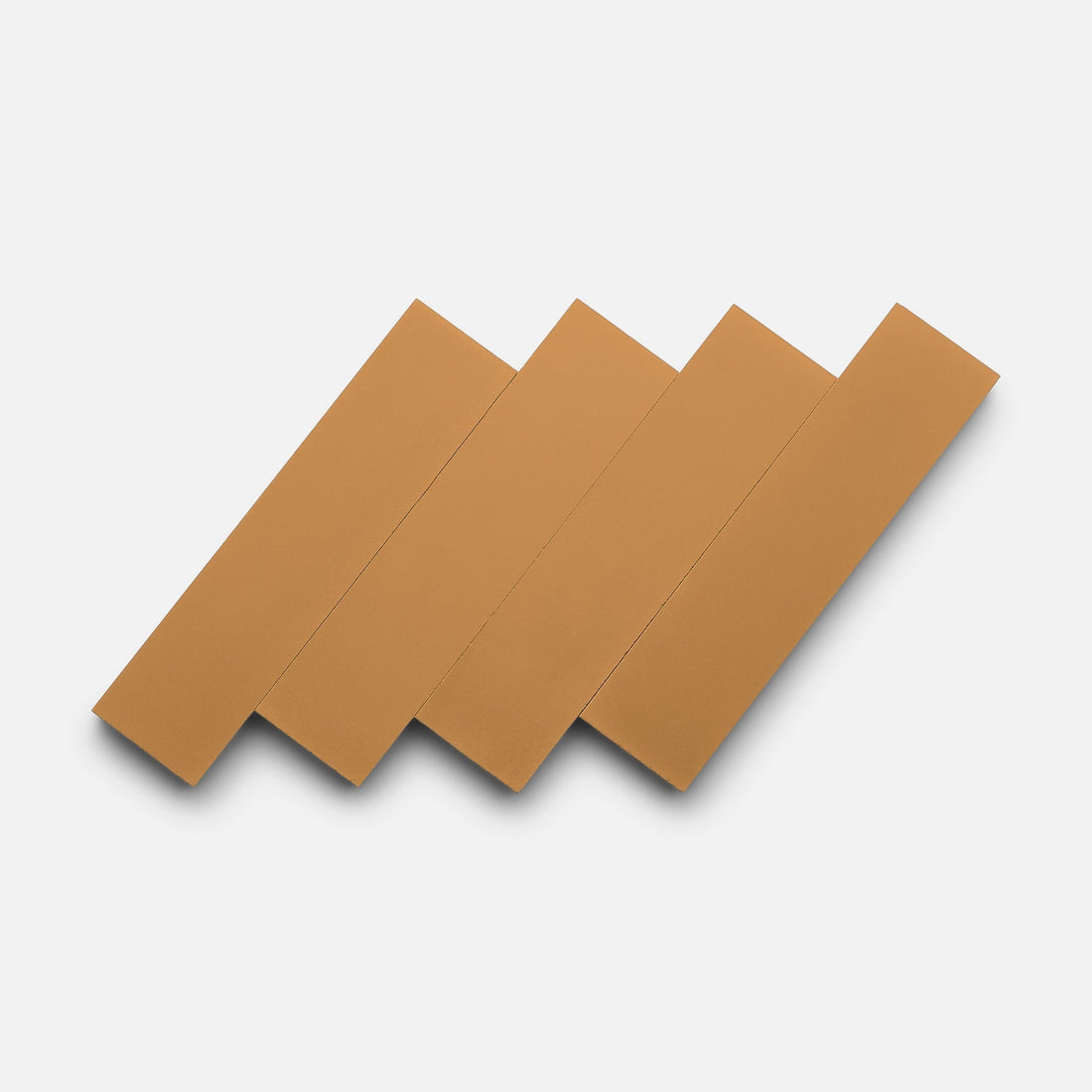 Four rectangular Saddle 2x8 tiles by Zia Tile, with their tan hue and crisp lines, are arranged diagonally and overlapping on a plain white background, echoing the brand’s signature earthy tones and modern aesthetic.