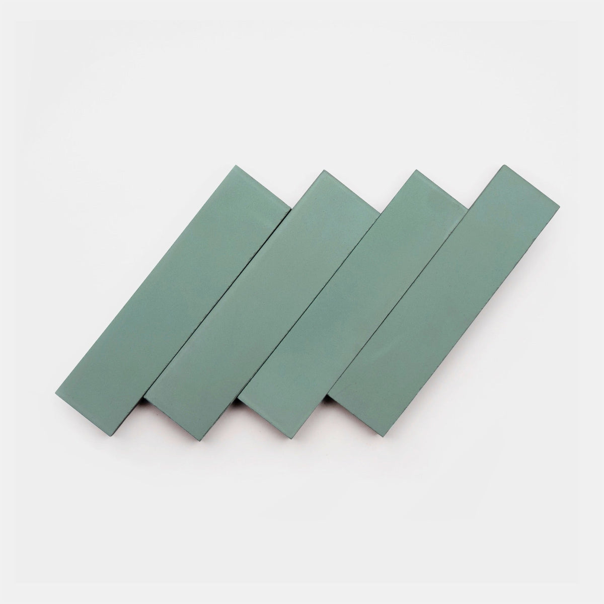 Four Saddle 2x8 tiles by Zia Tile, each rectangular and greenish-gray, are arranged diagonally in a staggered, overlapping pattern on a white background.