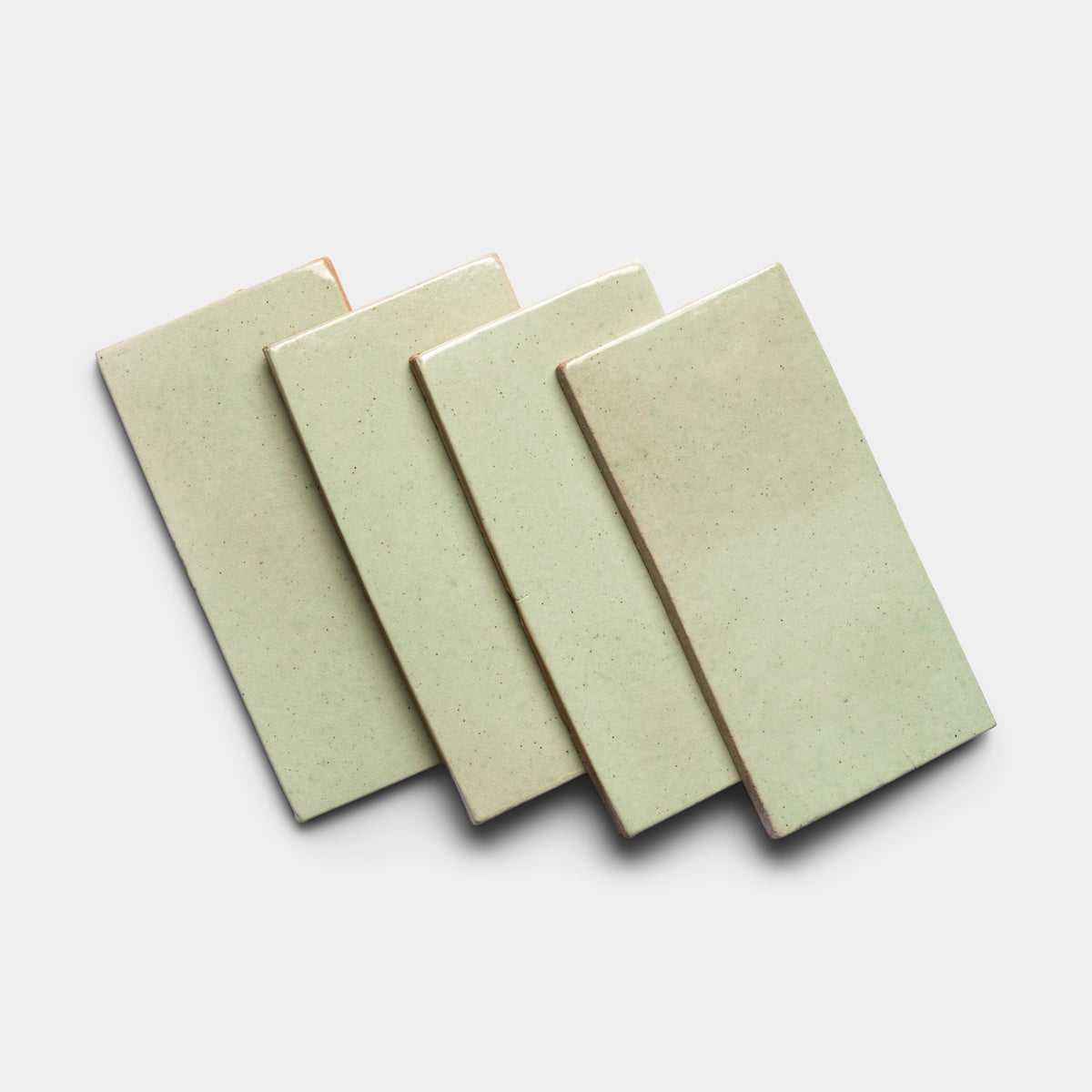 Four Sayulita 4x8 Rectangle tiles by Zia Tile, in light green ceramic, are arranged in a slightly overlapping diagonal row on a plain white background.