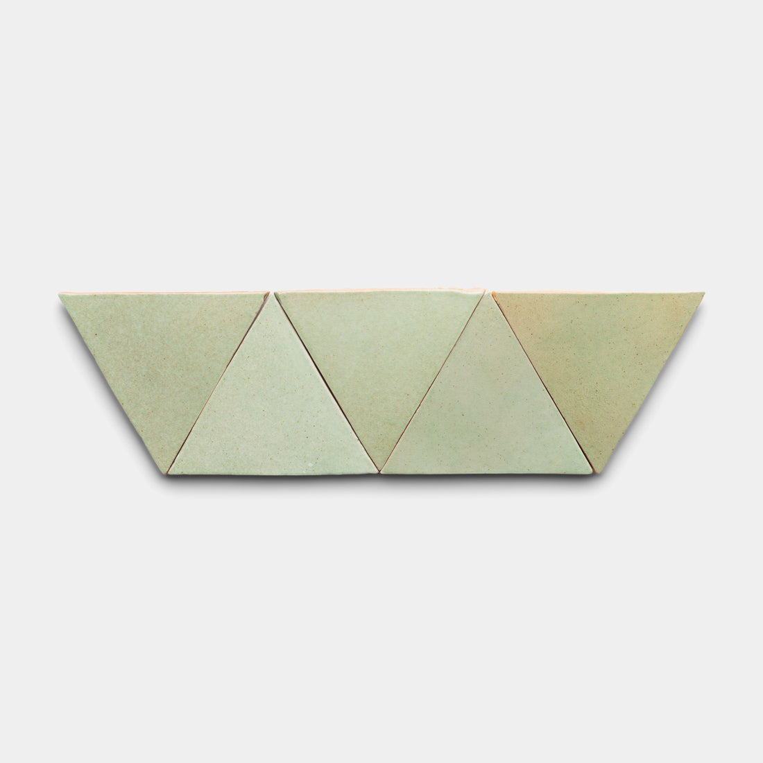 Four Sayulita Triangle tiles from Zia Tile in light green are arranged side by side in a straight row on a plain white background.