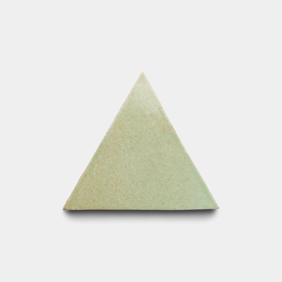 The Sayulita Triangle by Zia Tile is an equilateral, light green tile with a smooth finish, centered on a plain white background and casting a soft shadow below.