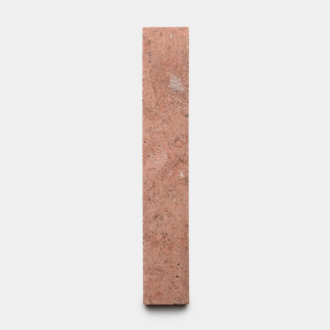 A single Sedona 2x12 brick by Zia Tile, featuring a reddish-brown rectangular shape, stands vertically against a plain white background.