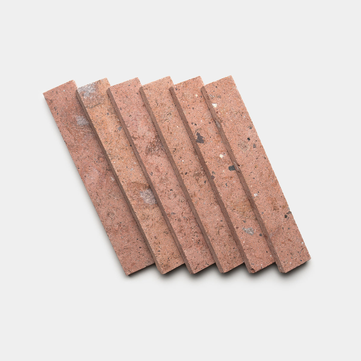 Six Sedona 2x12 bricks by Zia Tile, featuring a reddish-brown hue and slightly rough texture with small dark and light spots, are arranged side by side in a diagonal row against a white background.