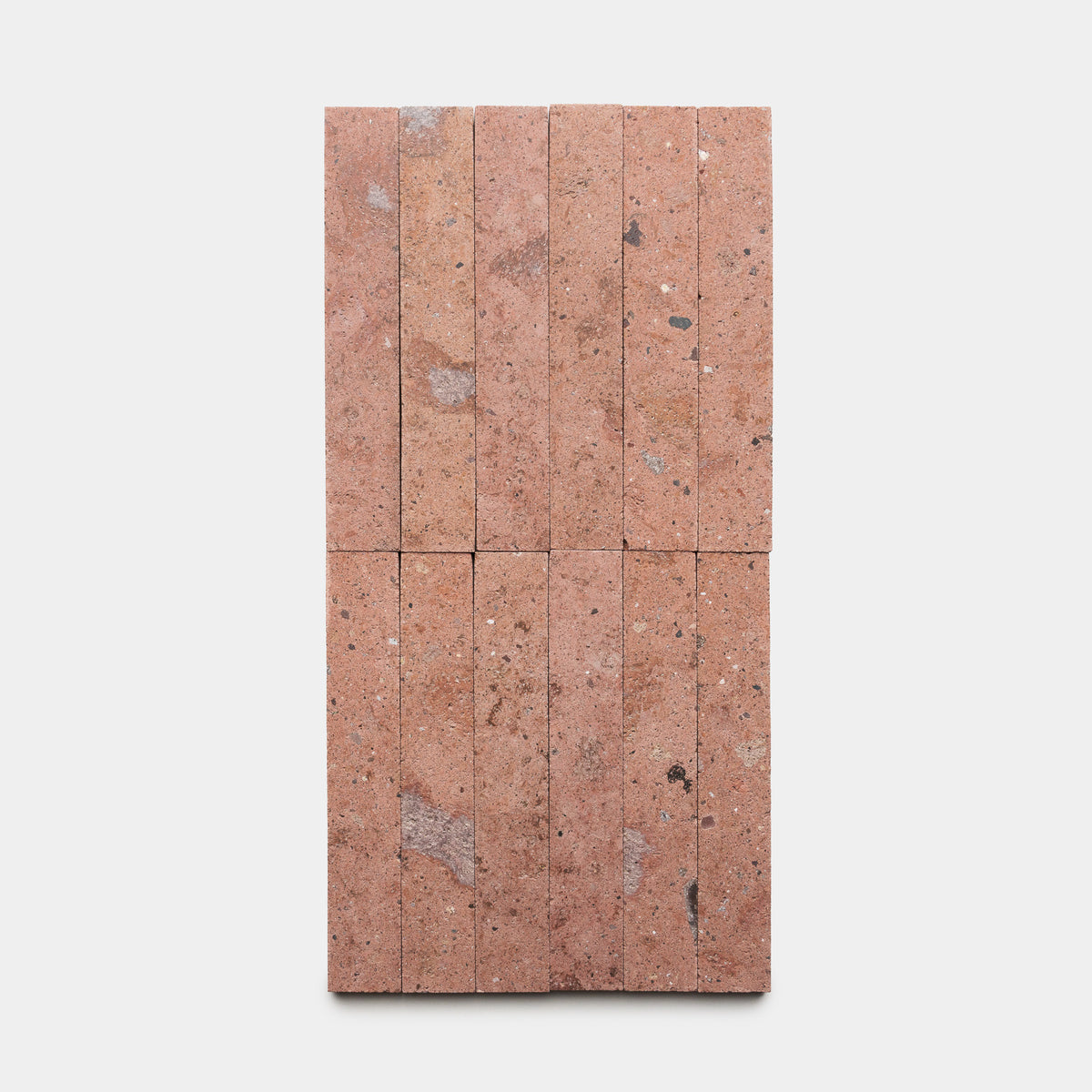 Sedona 2x12 bricks by Zia Tile, featuring a pinkish hue with gray and black specks, are arranged vertically in two rows on a plain white background.