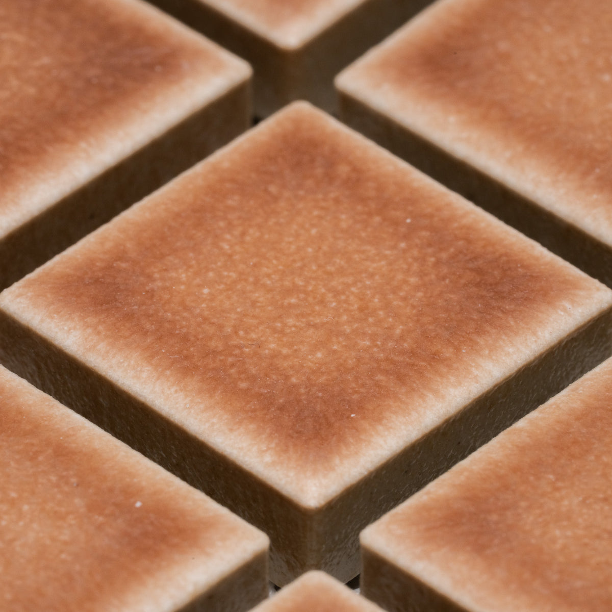Close-up of Zia Tile’s Sepia 1x1 tiles: brown, square tiles set in a grid with subtly rounded edges and a matte, textured finish. Lighting highlights their dimensional, raised effect.