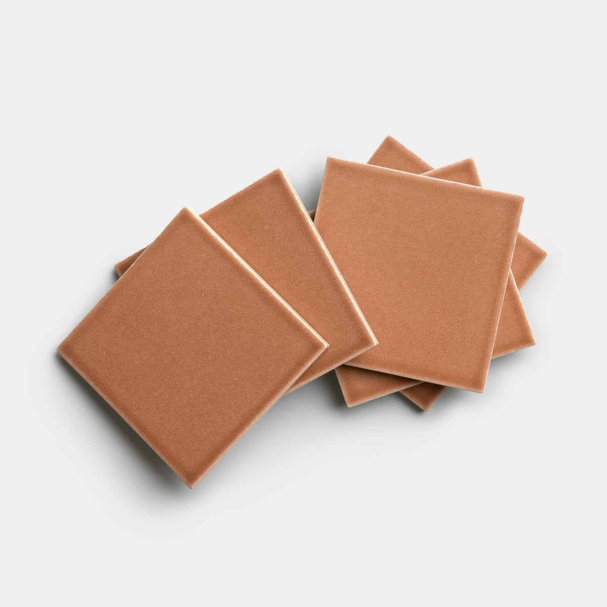 Six Sepia 4x4 ceramic tiles by Zia Tile, in light brown, are arranged in an overlapping, slightly fanned-out pattern on a white background.