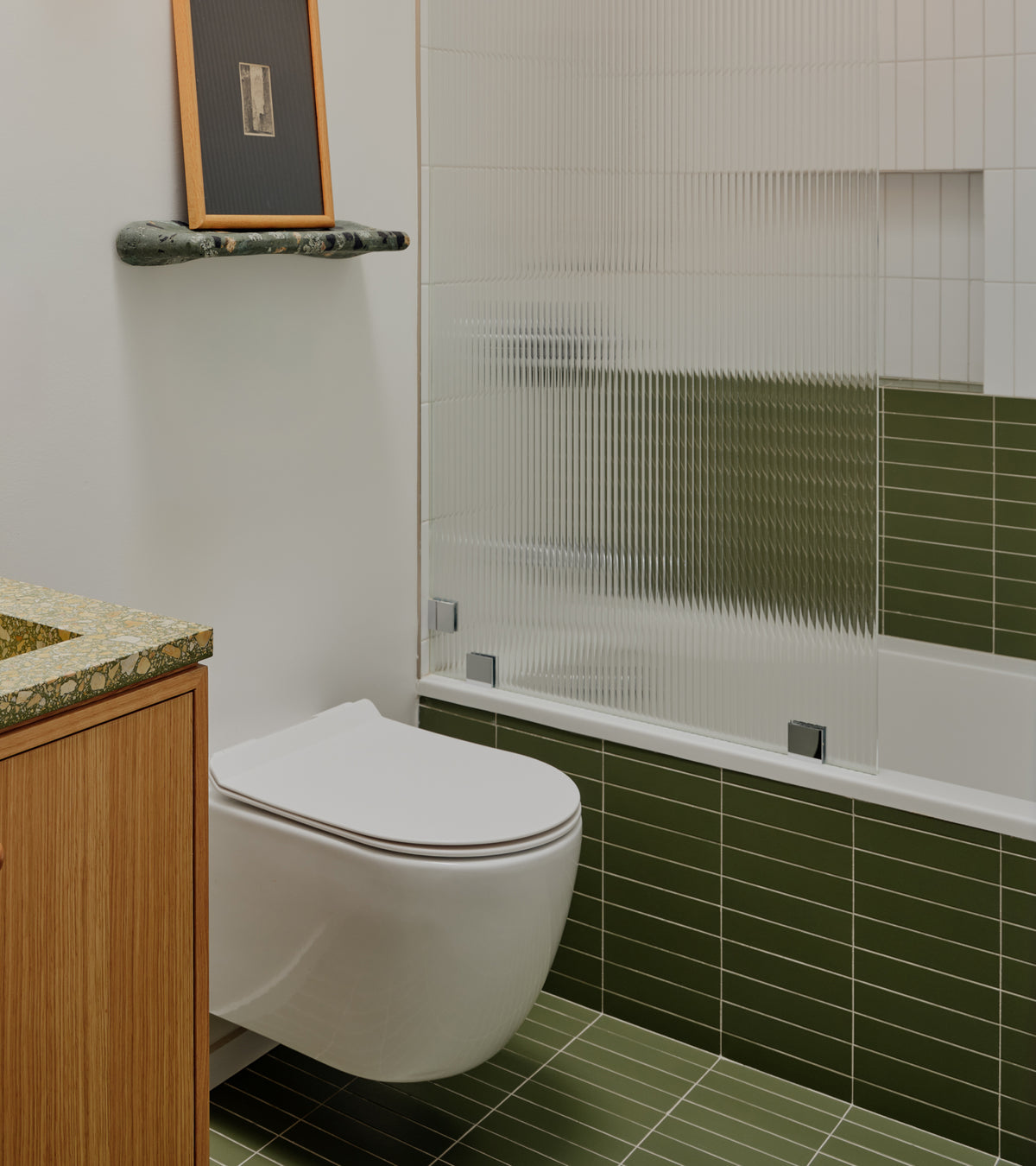 Bathroom featuring olive green Sequoia 2x8 matte ceramic tiles on the walls and floors, with a wall-mounted toilet and a fluted glass shower screen.