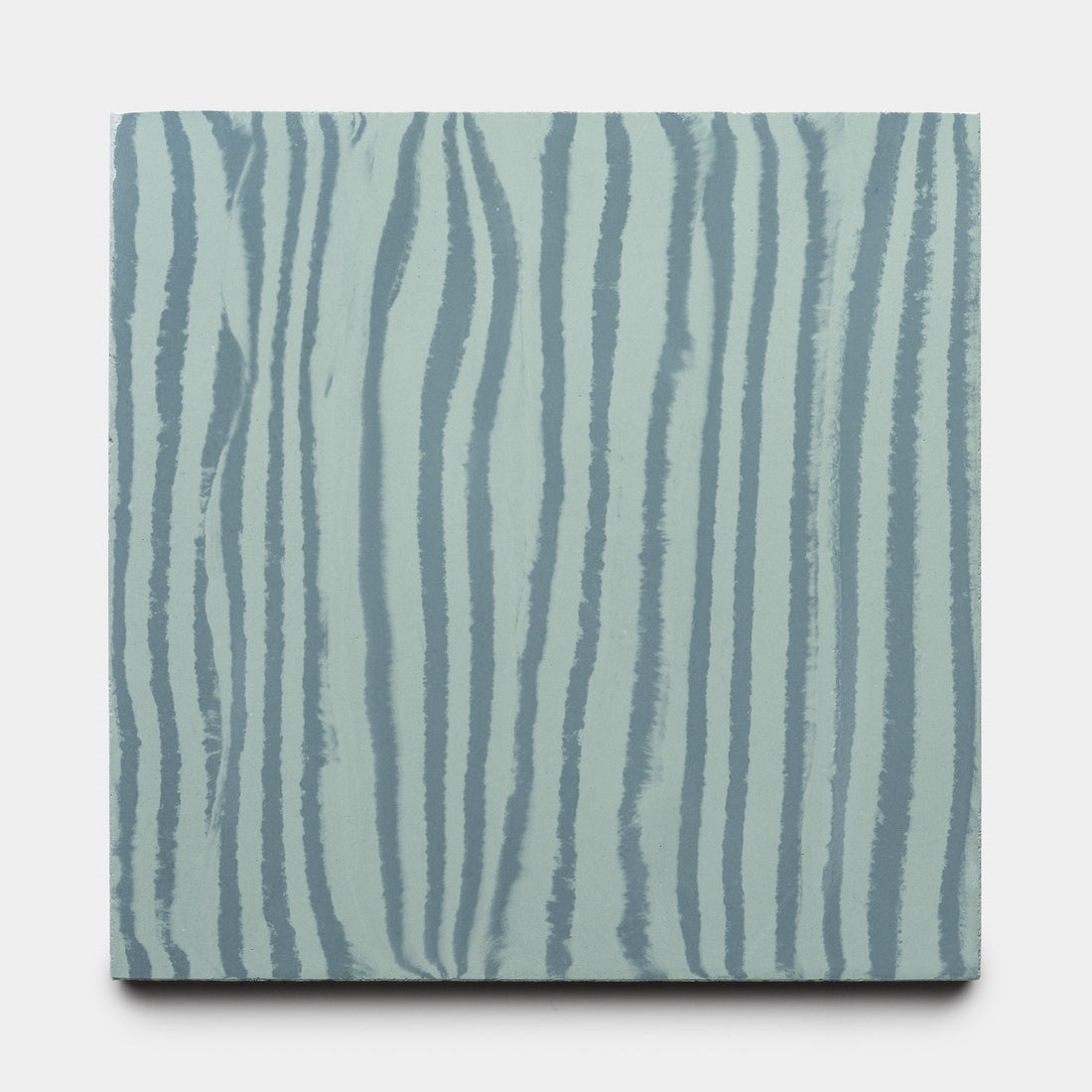 The Zia Tile Shoreline Slate + Sage 8x8 is a square tile with a light blue background and vertical, wavy darker blue stripes reminiscent of wood grain, offering a simple and abstract design.