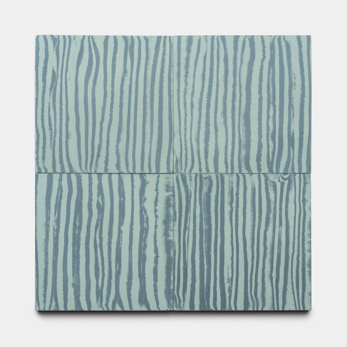 The Shoreline Slate + Sage 8x8 tile by Zia Tile features a square design with horizontal division and vertical wavy stripes in light blue and gray, evoking a wood grain or marbled look on a plain white background.