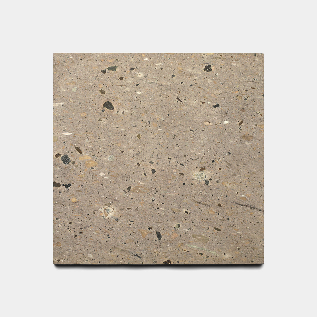 The Sierra 12x12 by Zia Tile is a square Mexican Cantera tile, featuring a light brown base with dark and light speckles for a terrazzo-like look, crafted from natural volcanic stone and shown on a plain white background.