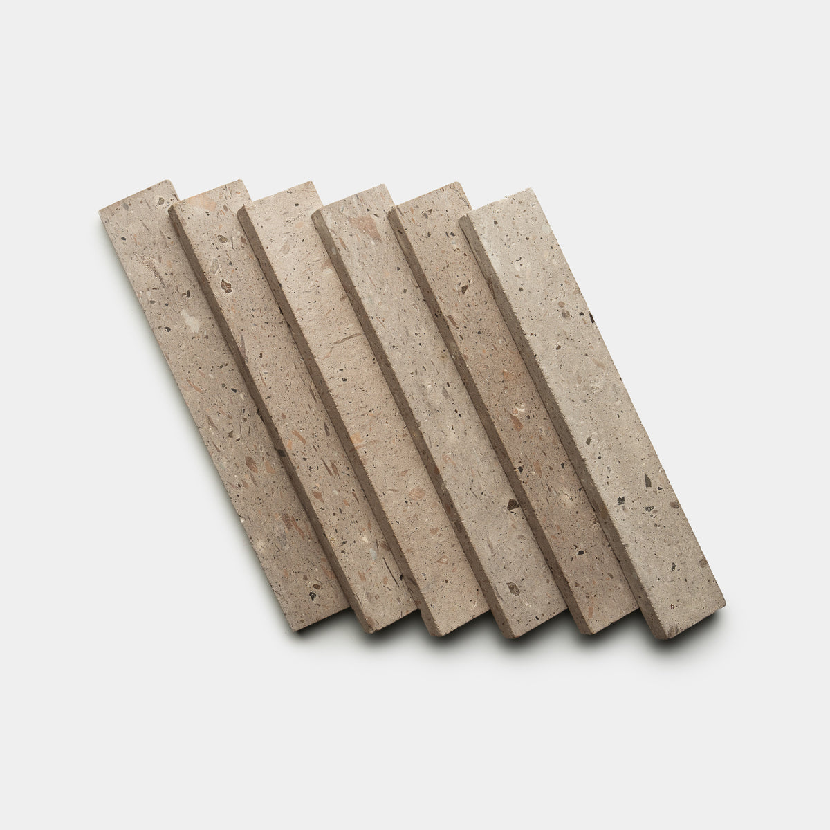 Six Sierra 2x12 tiles by Zia Tile, rectangular and beige with speckled, textured surfaces, are arranged diagonally in a staggered, overlapping pattern on a plain white background.