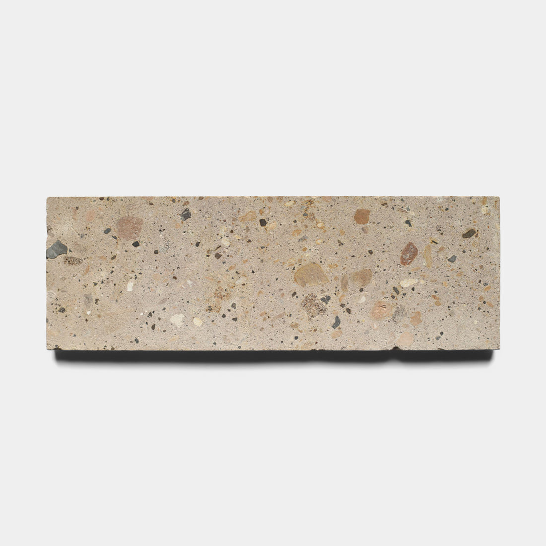 The Sierra 4x12 by Zia Tile is a rectangular beige Cantera stone tile crafted from natural volcanic stone with small multicolored chips embedded on its surface, displayed against a plain white background.