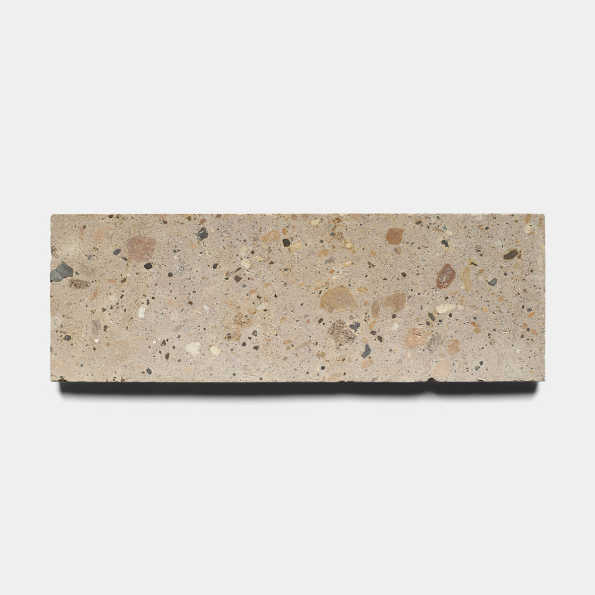 The Sierra 4x12 by Zia Tile is a rectangular beige Cantera stone tile crafted from natural volcanic stone with small multicolored chips embedded on its surface, displayed against a plain white background.