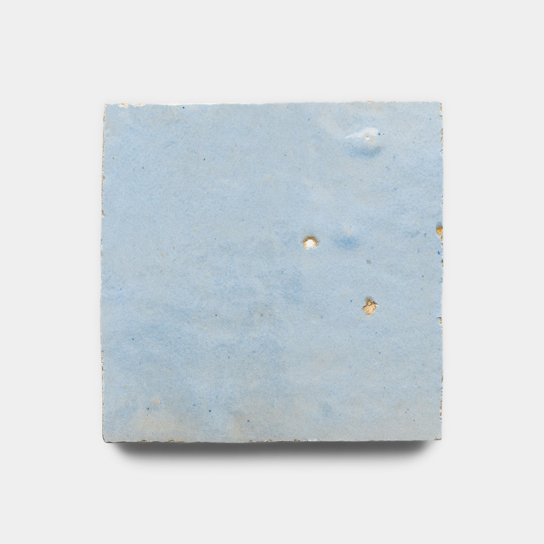 The Skylight 4x4 by vendor-unknown is a square ceramic tile with a light blue, matte, gently textured surface, inspired by Moroccan zellige. Subtle variations and two small holes make it perfect for a unique kitchen backsplash. Shown on a white background.