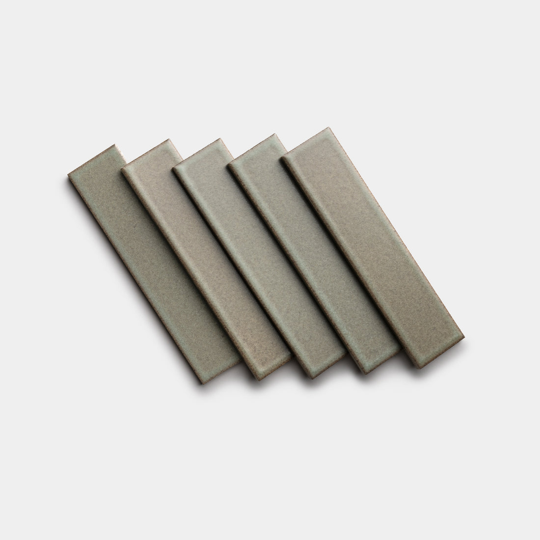 Five rectangular Spanish Moss 2x8 ceramic tiles from Zia Tile, gray in color, are arranged in a slightly fanned-out pattern on a plain white background.