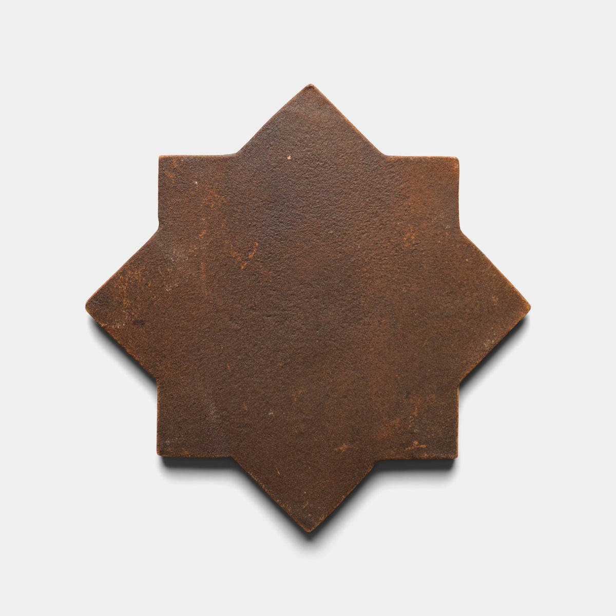 The Zia Tile Stars & Cross + Madera Sample, a brown, eight-pointed star-shaped handmade tile with a textured surface, is displayed on a plain white background.
