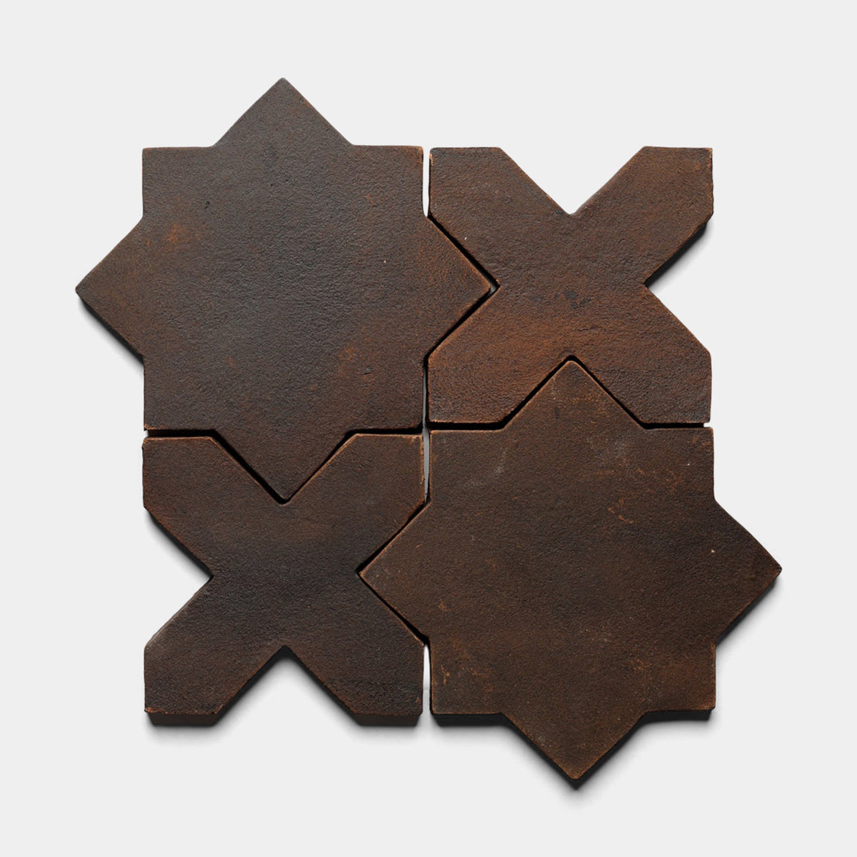 The Stars & Cross + Madera, Sample by Zia Tile features four brown matte ceramic tiles—two 8-pointed stars and two X-shapes—forming a geometric pattern on a light gray background, ideal for handmade or cement tile style lovers.