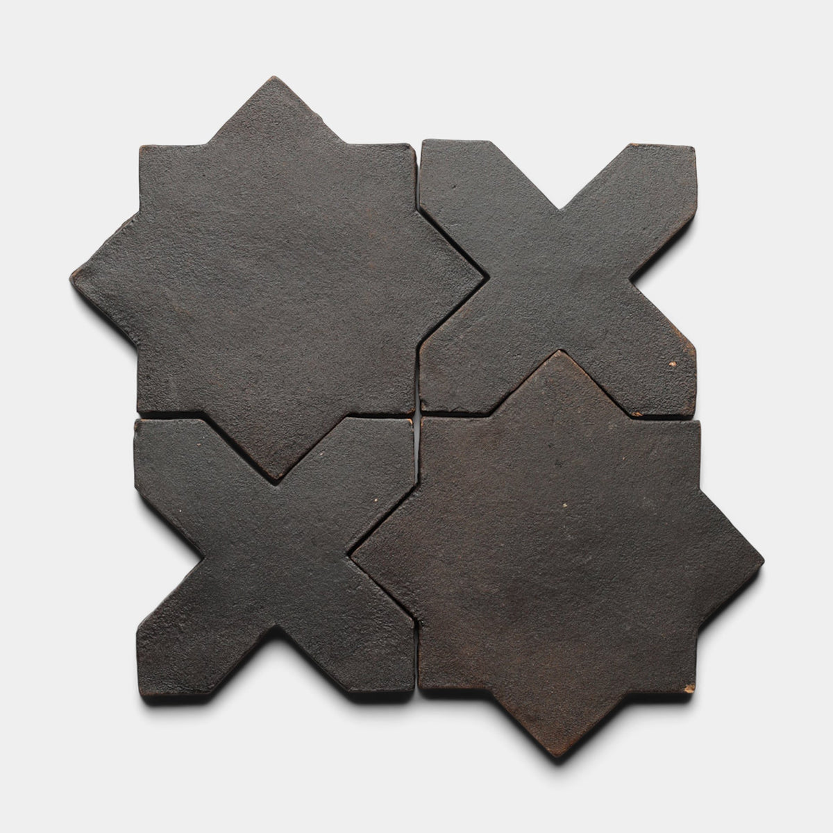The Stars & Cross + Oscura sample from Zia Tile features four dark, matte ceramic tiles—two X-shaped and two eight-pointed stars—arranged in a square on a white background, evoking the look of handmade artisan tiles.