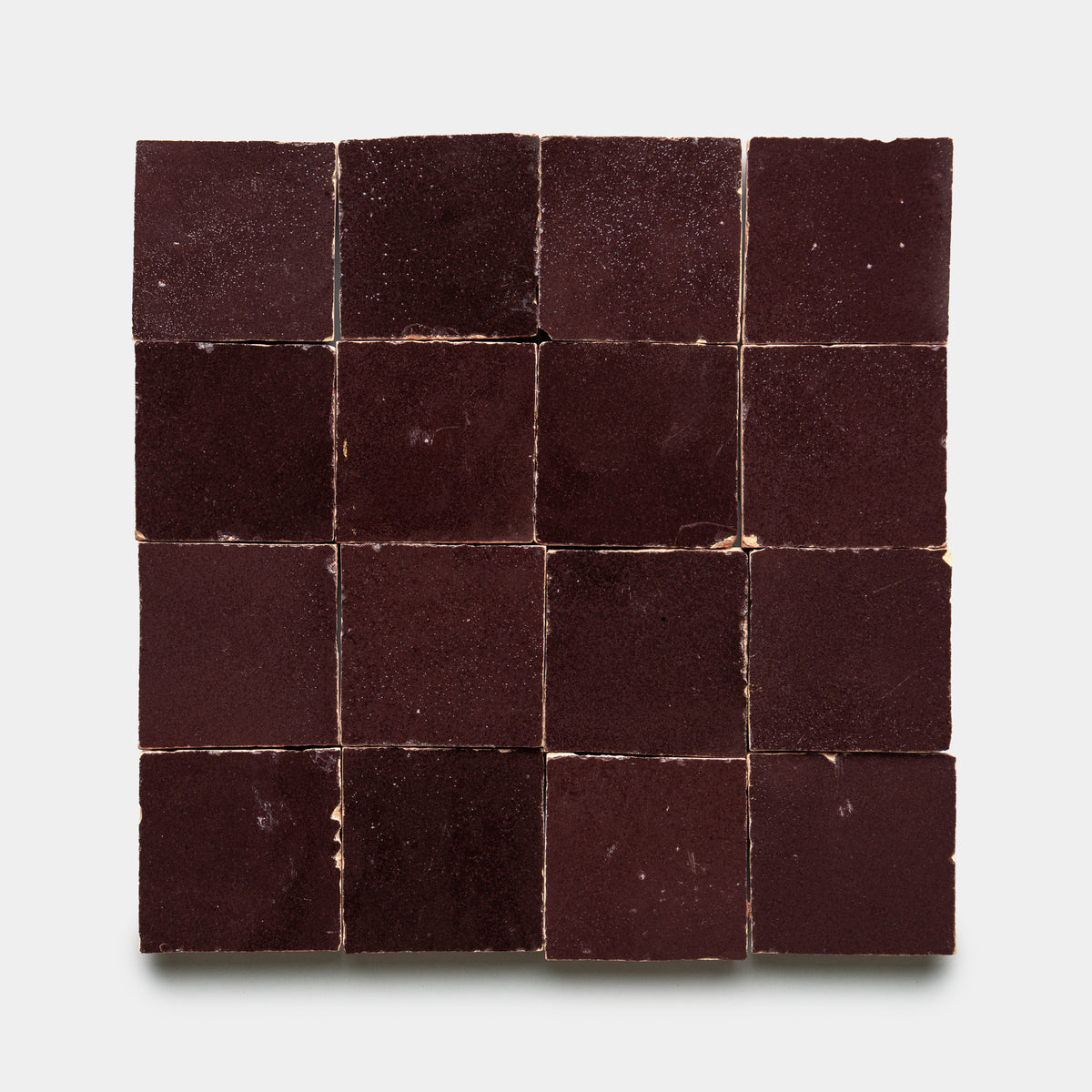 A 4x4 grid of sixteen Sumac 2x2 tiles by Zia Tile, featuring a dark brown textured finish, is displayed neatly arranged against a plain white background.