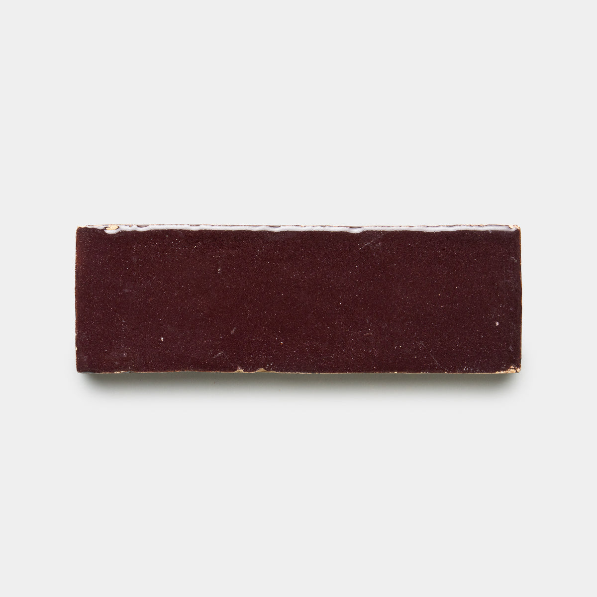 A rectangular Sumac 2x6 bar from Zia Tile rests on a plain white background. Its smooth, glossy surface features minor imperfections near the edges.