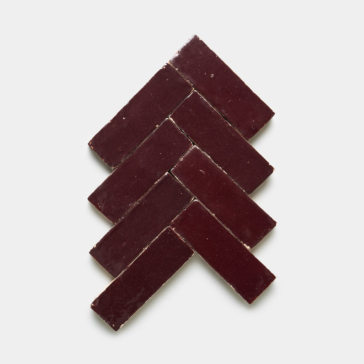 Eight Sumac 2x6 tiles from Zia Tile, in a rectangular dark reddish-brown hue, are laid in a herringbone pattern on a white background, creating an arrow or tree-like shape.