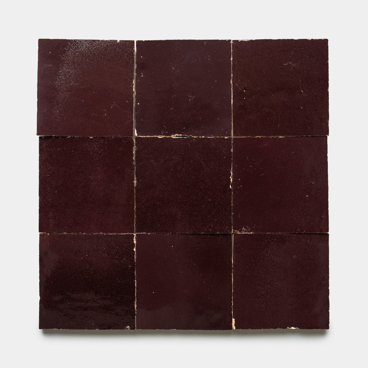 Nine Sumac 4x4 tiles by Zia Tile, dark burgundy and square, arranged in a 3x3 grid with slight gaps and visible imperfections, displayed on a plain white background.