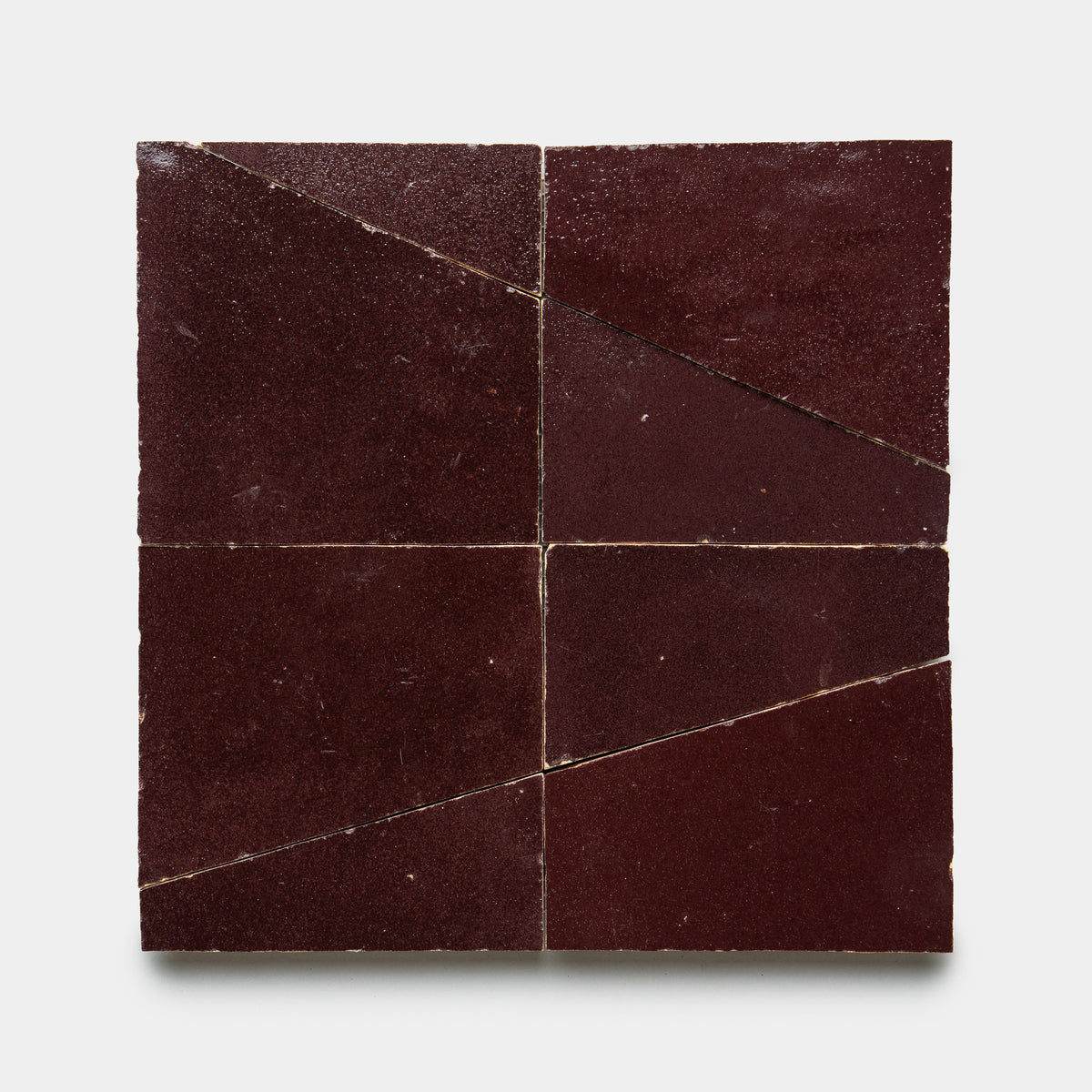 Atlas 1 by Zia Tile features four square burgundy tiles in a grid, each with a diagonal cut that forms two triangles. The tiles have a slightly textured surface and create an abstract geometric pattern when arranged together.