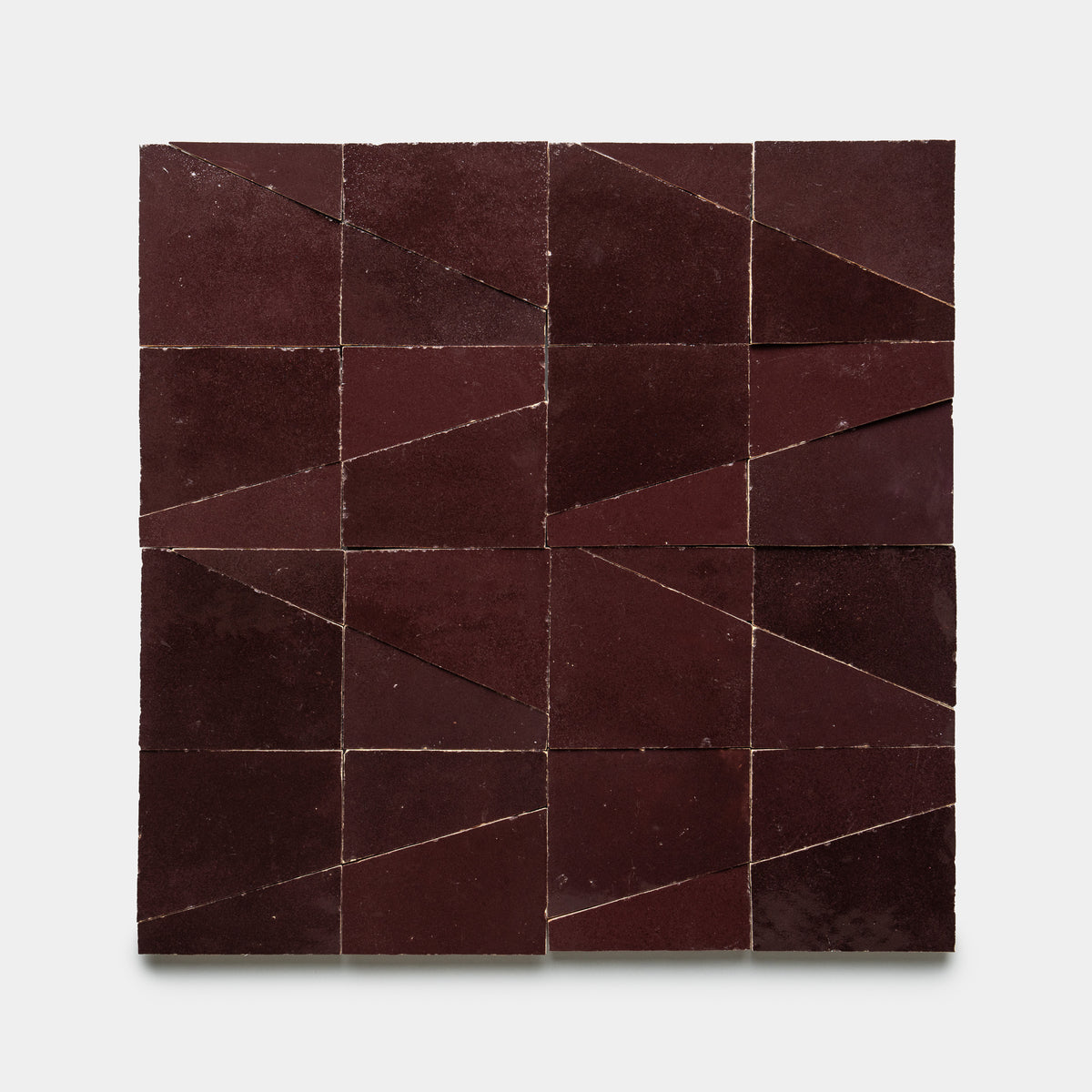 Atlas 1 by Zia Tile features a square grid of deep burgundy tiles, each split into geometric shapes that create an abstract, angular pattern on a plain white background.