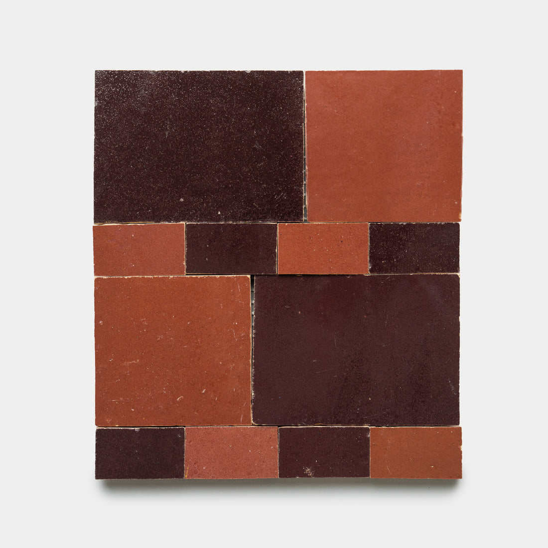 The Xylem 1 tiles by Zia Tile feature a square layout of red and dark brown rectangular and square tiles, creating a striking geometric pattern on a light gray background.