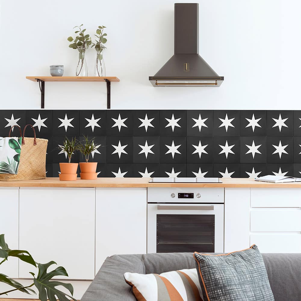 A modern kitchen with white cabinets, a wooden countertop, potted plants, a range hood, a straw bag on the counter, and a handmade black-and-white star-patterned tile backsplash using Super Nova 8x8 by vendor-unknown.