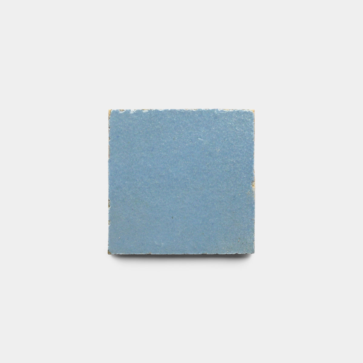 The Zia Tile Superior Blue 2x2 sample is a square ceramic tile featuring a smooth, muted blue surface with subtly worn edges, reminiscent of handmade tiles, shown against a plain white background.