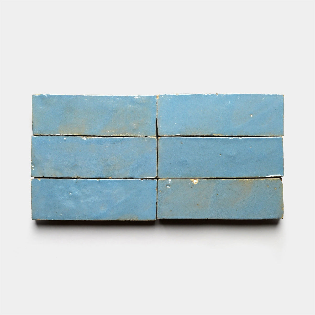 Six Superior Blue 2x6 sample tiles from Zia Tile, featuring a handmade look with slightly worn, uneven surfaces, are arranged in two rows of three on a plain white background.