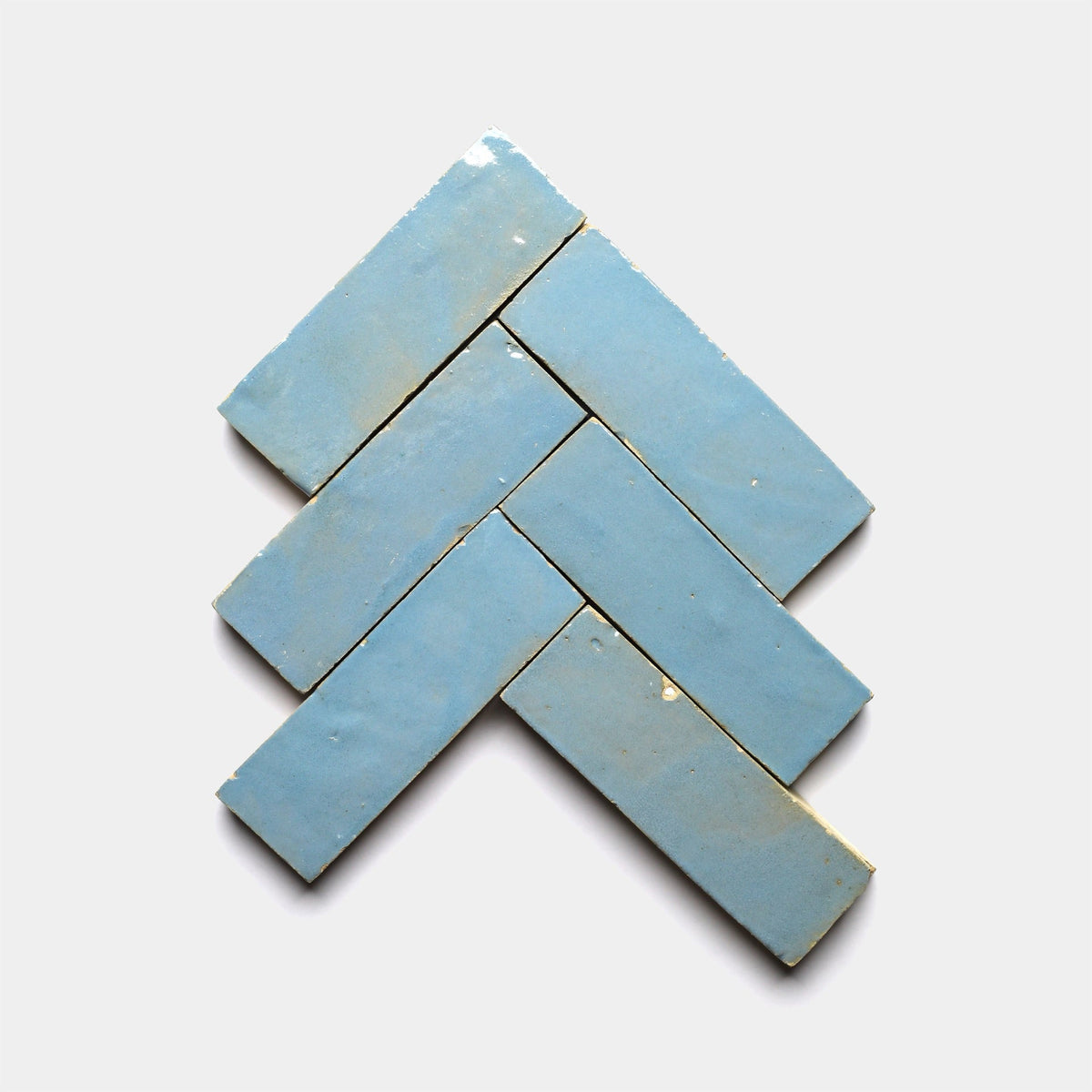 Five Superior Blue 2x6 sample tiles by Zia Tile, in a light blue shade, are displayed in a herringbone pattern on a plain white background.