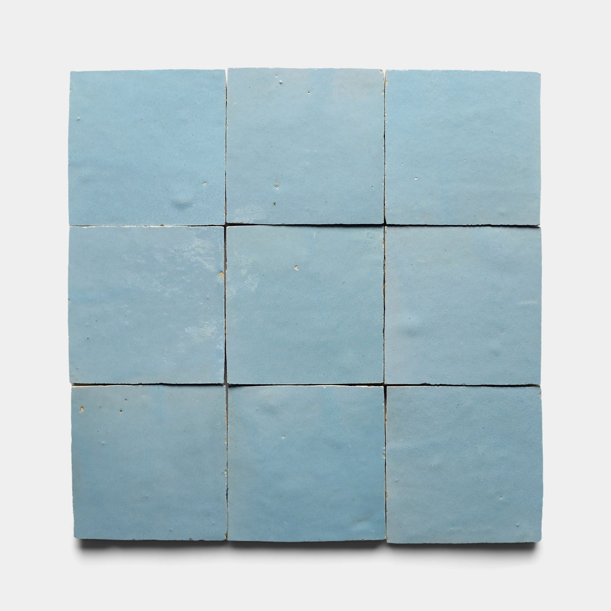 A sample of Zia Tile's Superior Blue 2x6 tiles is shown arranged on a white background, highlighting their light blue hue, handmade charm, subtle color variations, and slightly uneven surfaces.