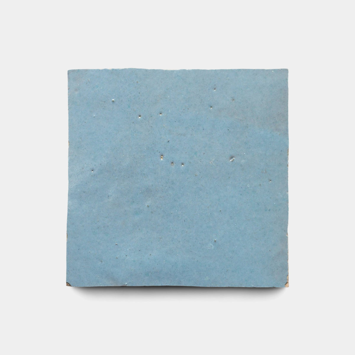 The Superior Blue 2x6 sample by Zia Tile is a single ceramic tile with a smooth, matte light blue finish and subtle pinholes, evoking handmade craftsmanship, shown on a plain white background.