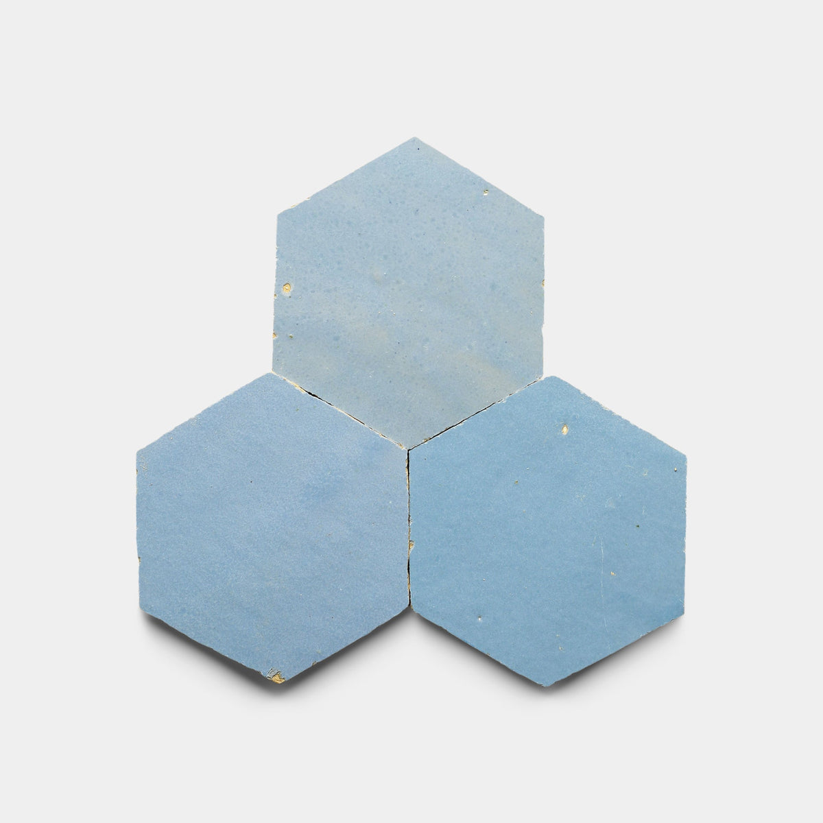 Three Superior Blue 2x6 tile samples by Zia Tile, in a hexagonal cluster on white, show off their matte finish and handcrafted charm with subtle irregular speckles.