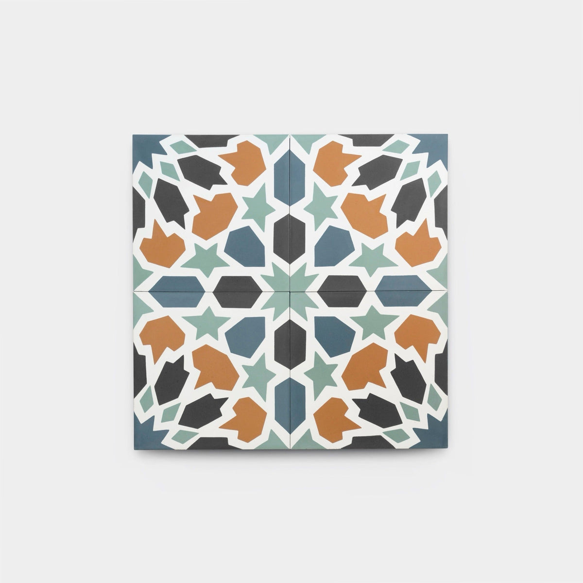 The Tangier 4x4 tile sample by vendor-unknown features a geometric, star-like pattern with orange, black, blue, and green shapes symmetrically arranged on a white background.