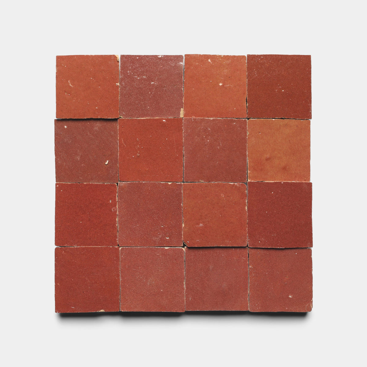 Sixteen Terra Rosa 2x2 tiles by Zia Tile are displayed in a 4x4 grid on a white background. Each handmade cement tile features unique shade and texture variations, adding rustic character to the sample set.