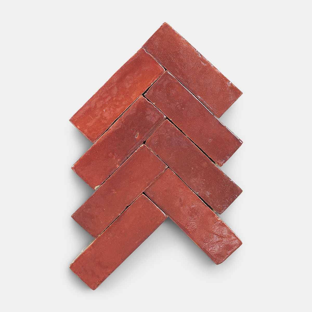 Six Terra Rosa 2x2 tiles from Zia Tile, in a rich red shade and handmade look, are arranged in a herringbone pattern on a white background, creating a striking geometric, arrow-like design.