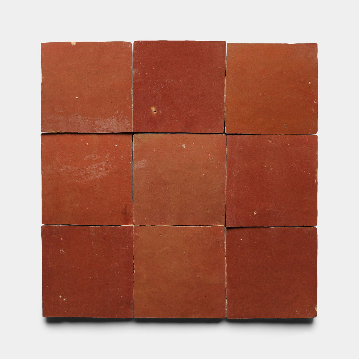 Nine handmade Terra Rosa 2x2 tiles by Zia Tile are arranged in a three-by-three grid on a light background. Their matte finish and subtle imperfections highlight the artisanal quality of each cement tile sample.