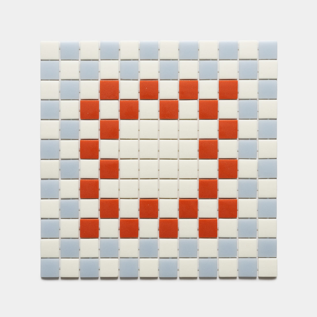 The Zia Tile Tesserae Milk + Tranquil Blue + Roma sample features a red heart made from mosaic squares, surrounded by white and light blue tiles in a grid pattern on a plain background.