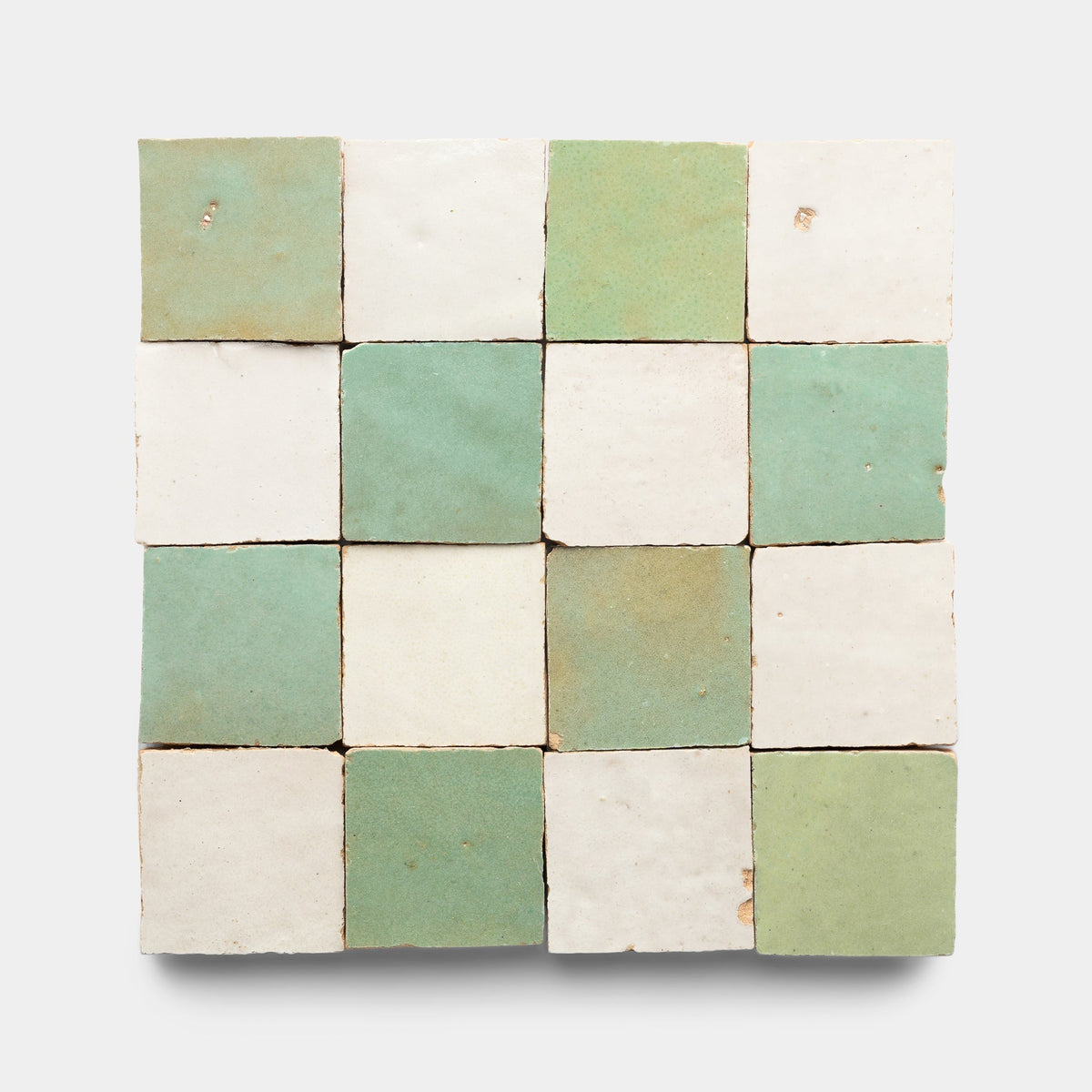 The Tidepool + Casablanca Checkerboard Sample by Zia Tile features sixteen handmade tiles in a 4x4 grid, alternating pale green and off-white, each with unique imperfections and a rustic texture.