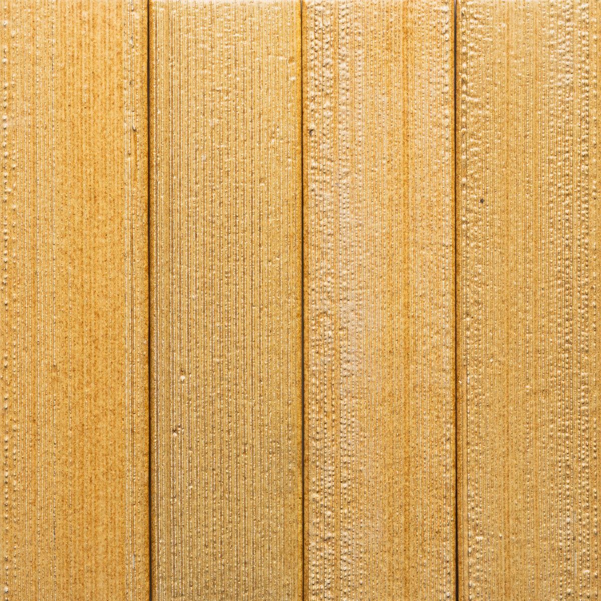 Close-up of Toast + Etched, Sample by Zia Tile—a wooden surface with a vertical plank pattern, light brown color, visible grain texture, and varied shades that highlight the natural wood finish.