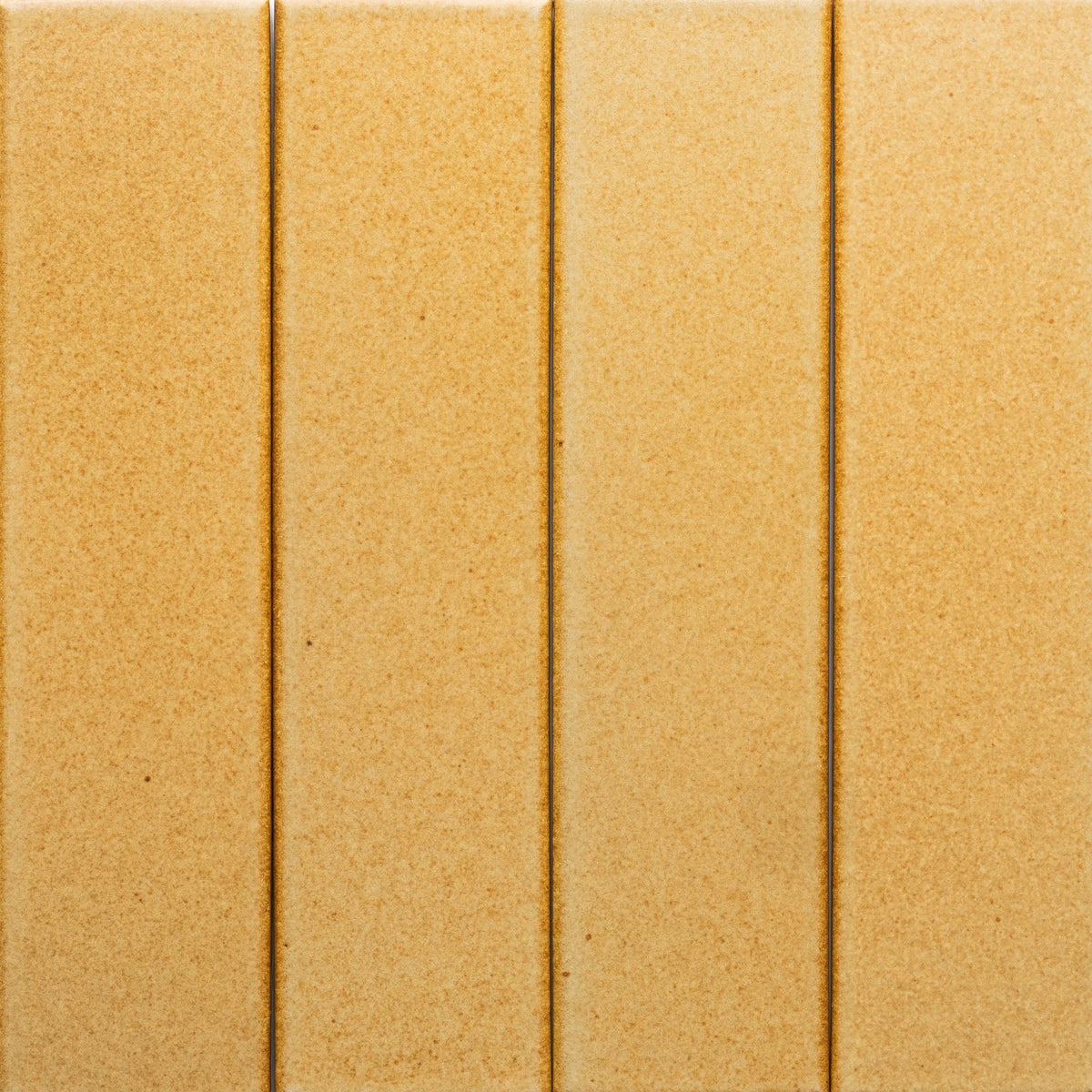 Four vertical Toast + Flat, Sample tiles by Zia Tile are closely arranged side by side. Each light brown ceramic tile is rectangular with subtle grooves in between and features a smooth, evenly colored finish.