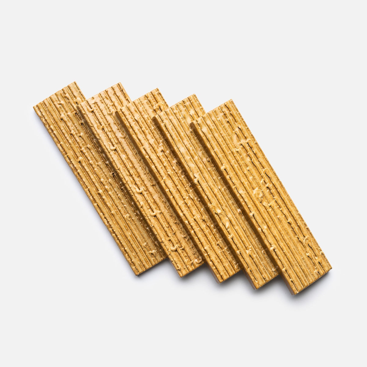 Five rectangular Toast + Furrowed, Sample tiles by Zia Tile are arranged in a fanned-out pattern on a white background. The tiles have a golden-brown color and a textured, ridged surface.