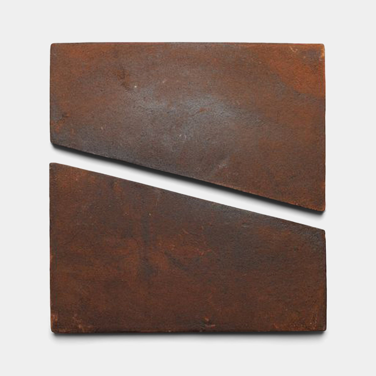 Two rusty, rectangular metal plates arranged on a white background evoke the artisanal style of Zia Tile’s Toltec + Madera sample, with one diagonally split and offset below for a striking visual effect.