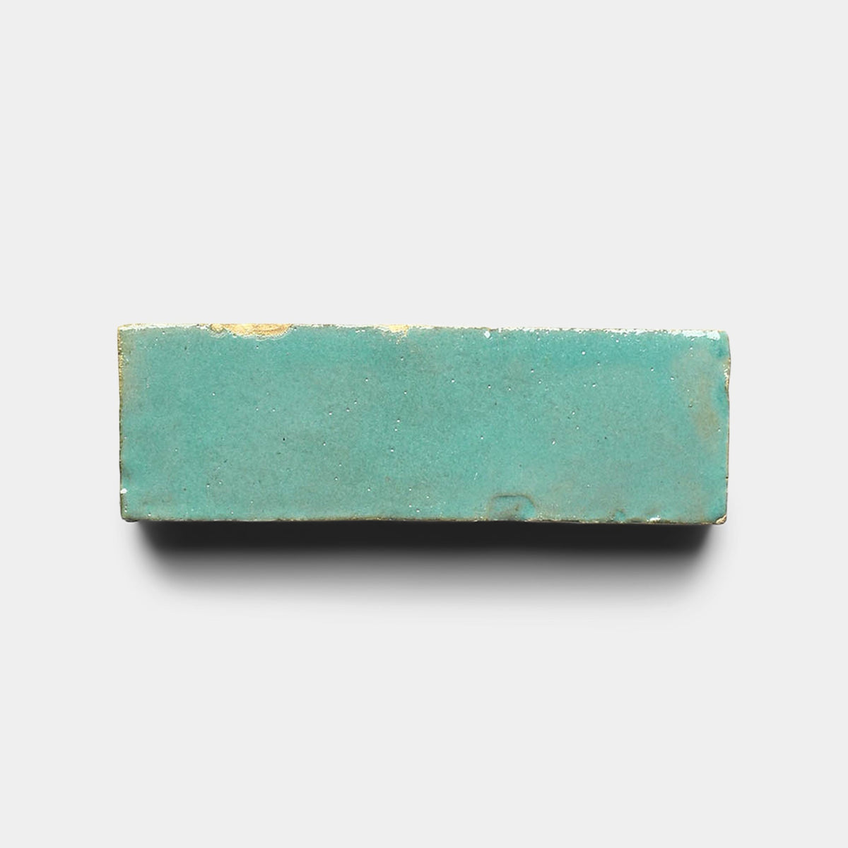 The Tulum 2x2 Sample by Zia Tile is a handmade, rectangular turquoise ceramic tile with a glossy finish and subtle yellowish spots, shown against a plain white background.